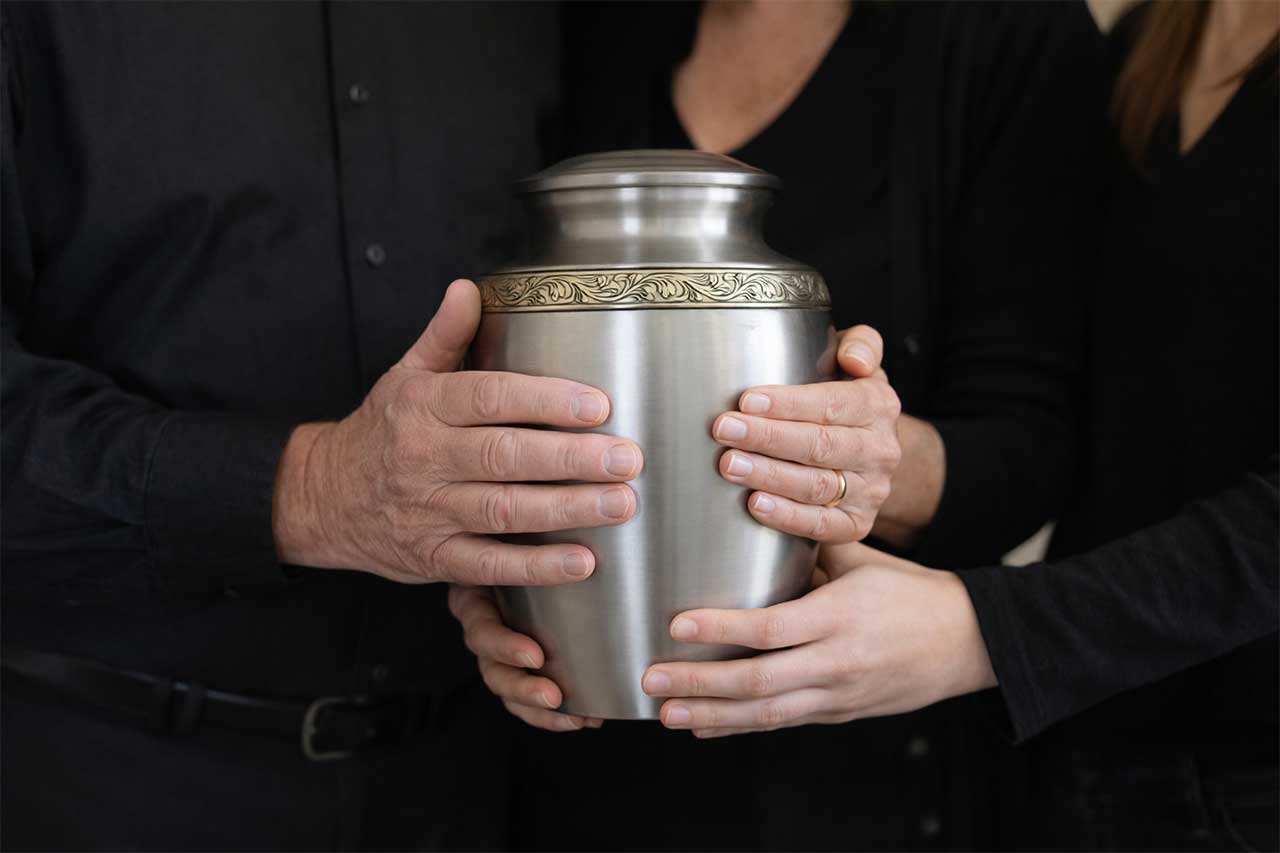 Family members holding a metal cremation urn together
